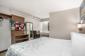 Een hotelkamer met een bed, een televisie, een magnetron, een koelkast en een spiegel.