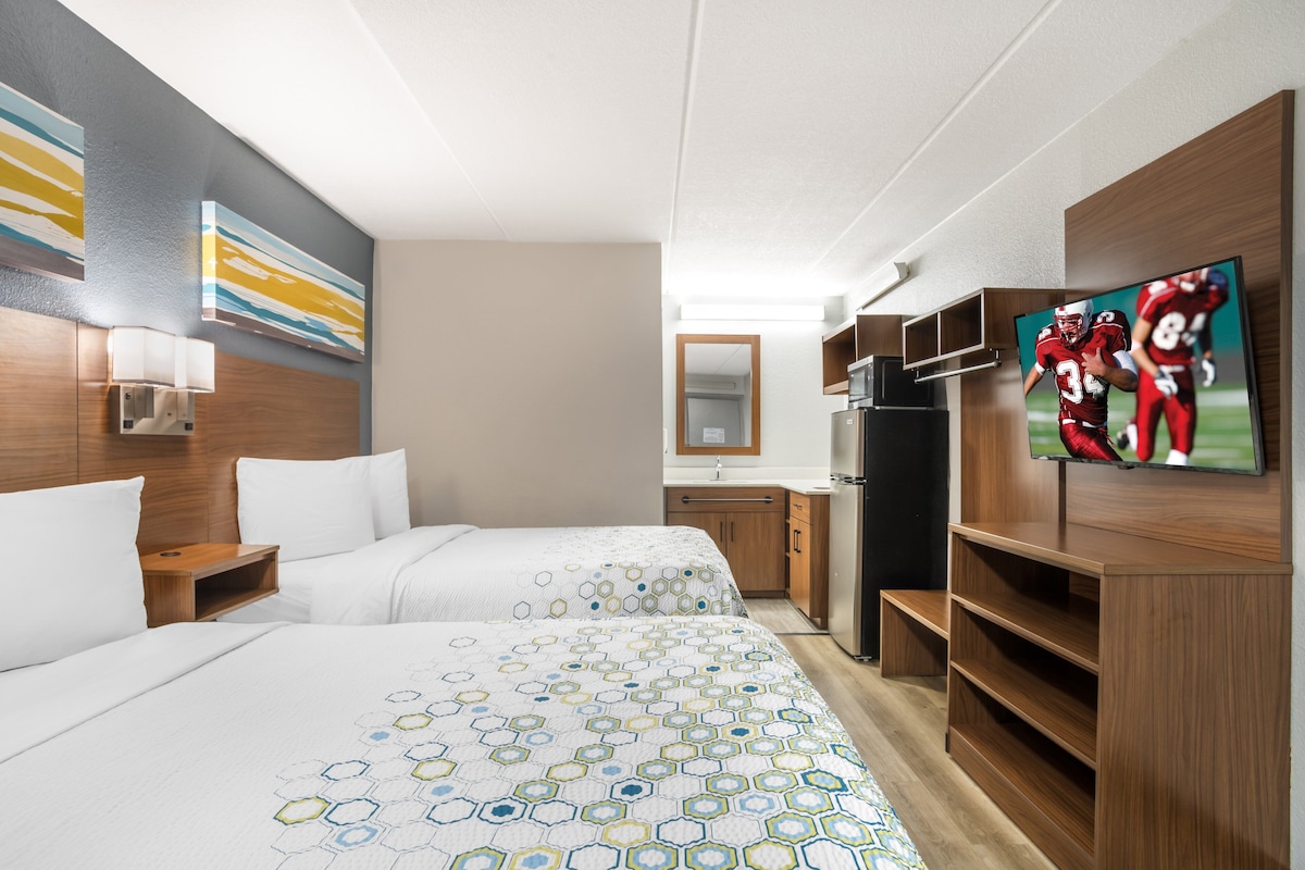 A hotel room with two beds, a TV, a refrigerator, and a wooden cabinet.