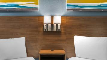A hotel room with two beds, a small wooden nightstand, and a wall-mounted light fixture.