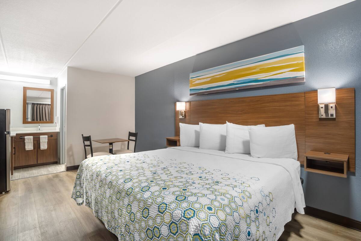 Une chambre d’hôtel avec un grand lit, une tête de lit en bois, une table de chevet, un bureau et une chaise.