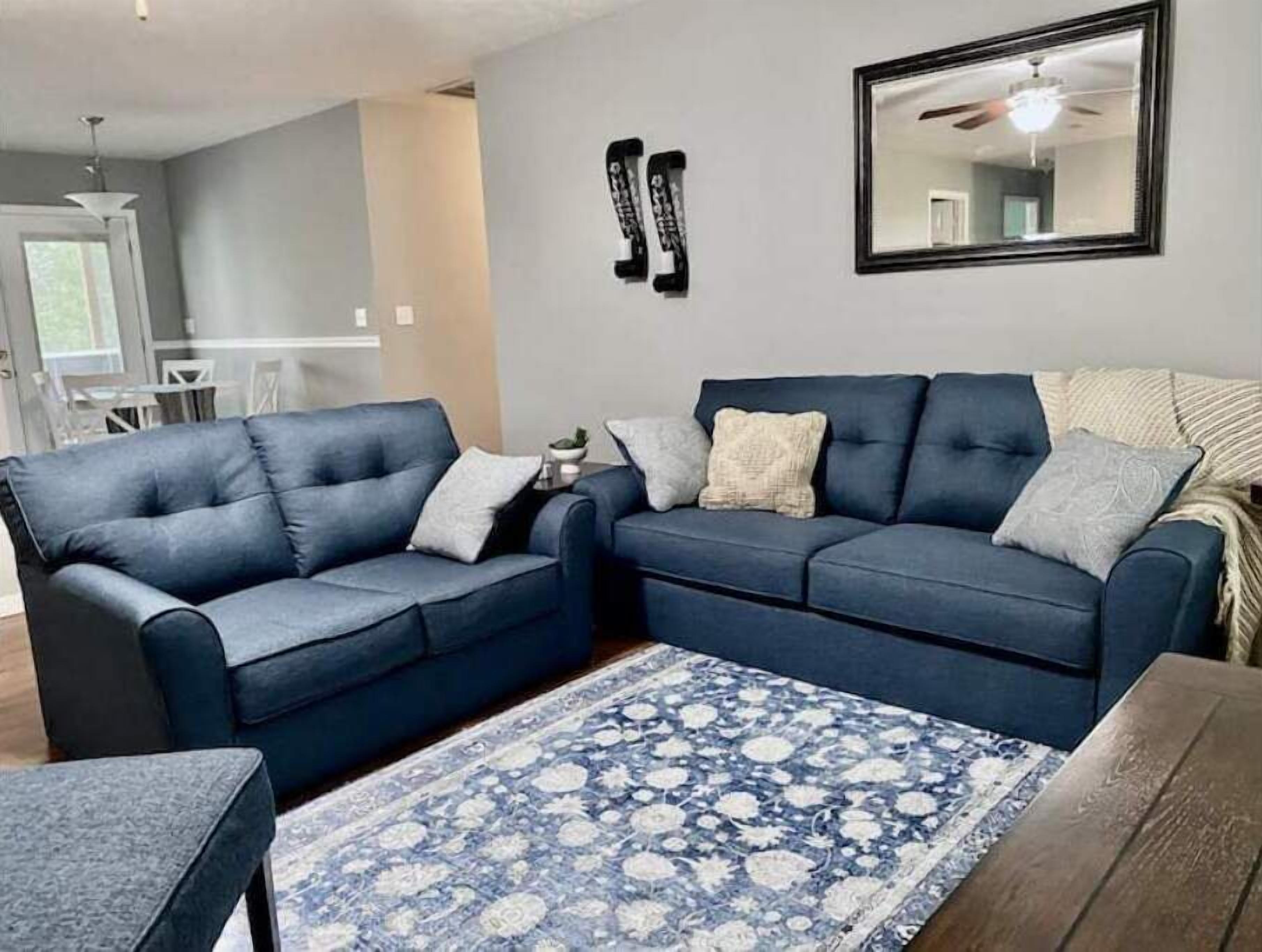 A living room with two blue sofas, a patterned rug, and a mirror on the wall.