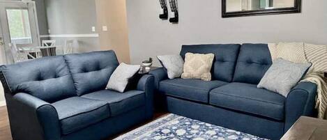 A living room with two blue sofas, a patterned rug, and a mirror on the wall.