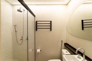 A modern bathroom with a glass shower enclosure, a toilet, and a sink with a mirror above. - Onze22 NR (São Paulo)