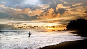 Ein Strandbild mit einer Person, die im Sonnenuntergang am Ufer entlanggeht.
