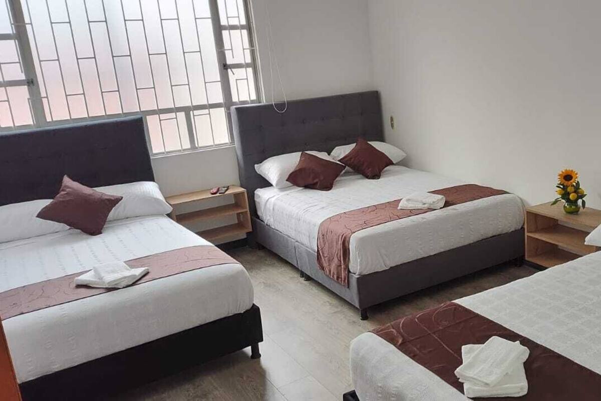 Habitación de hotel con tres camas, cada una con cabecera, y una mesita con un florero.