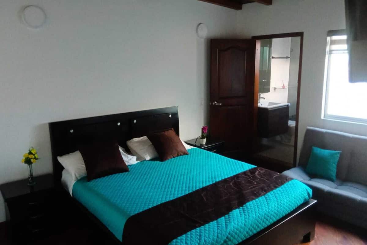 Un dormitorio con cama, mesita de noche, silla, puerta y ventana.