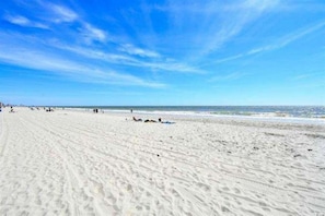 A wide sandy beach with footprints leading towards the ocean, under a clear blue sky.