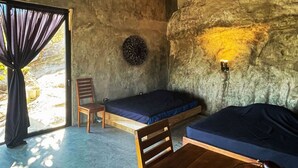 A rustic room with a bed, a chair, a table, and a fruit basket.