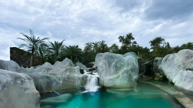 A pool with clear turquoise water, surrounded by large white rocks and palm trees. - Destino Hotel & Hot Springs Day Pass  (Fortuna)