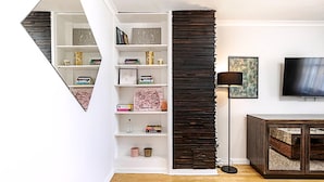 Un salon moderne avec une bibliothèque blanche, un mur d’accent en bois foncé, un lampadaire et un téléviseur.