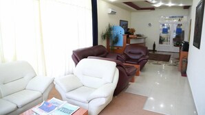 A reception area with a reception desk, two brown leather chairs, a white sofa, and a magazine on a table. - Hotel Apollonia (Pristina)