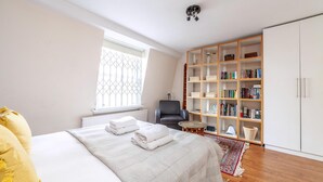 A bedroom with a bed, a bookshelf, a chair, and a radiator. - Stylish and Sleek Kensington Apartment (London)