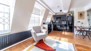 A modern kitchen with black appliances, a dining area with a wooden table and chairs, and a large window providing natural light. - Stylish and Sleek Kensington Apartment (London)