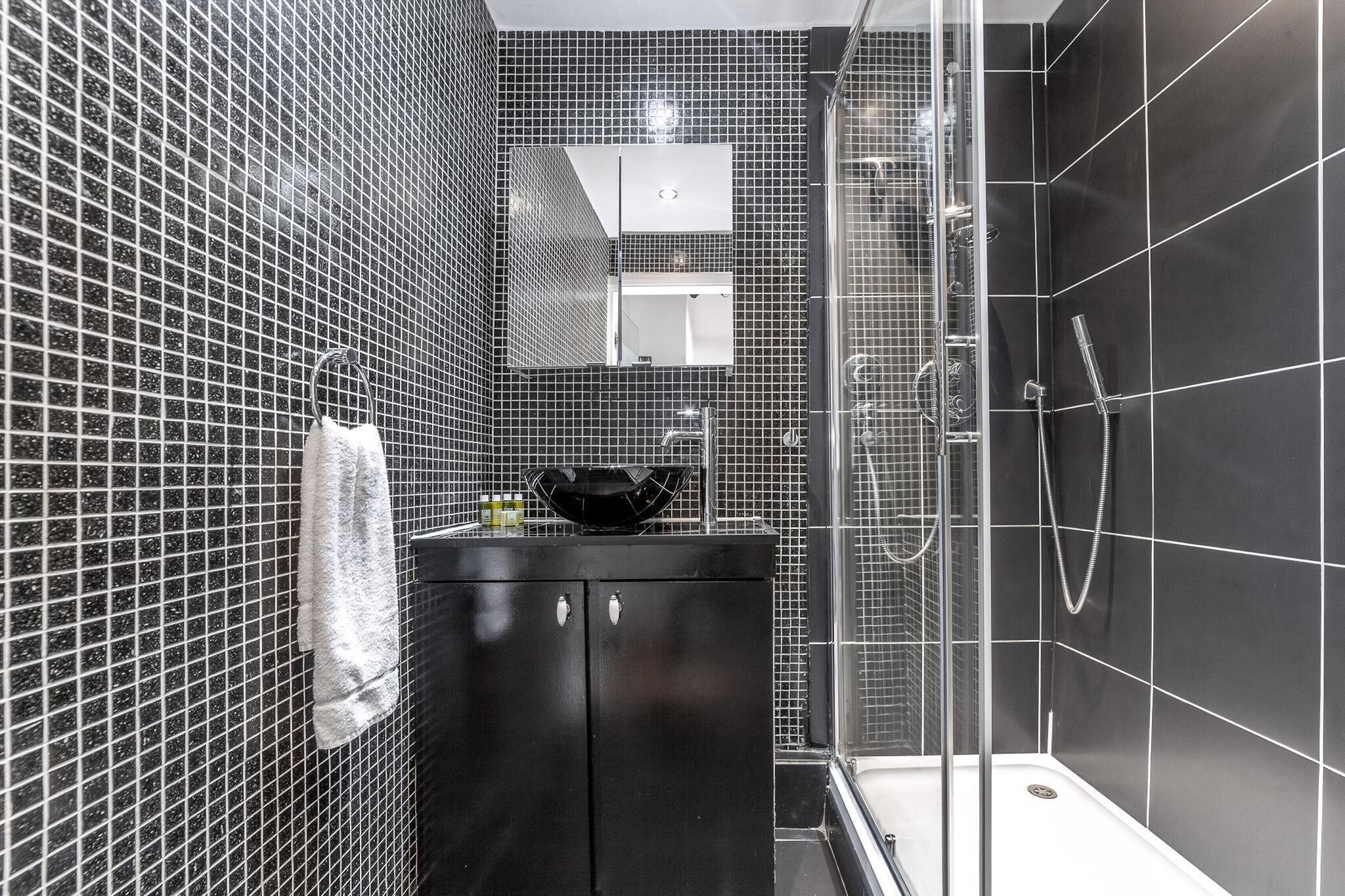 Un baño moderno con paredes de azulejos negros, un lavamanos negro y un box de ducha de vidrio.