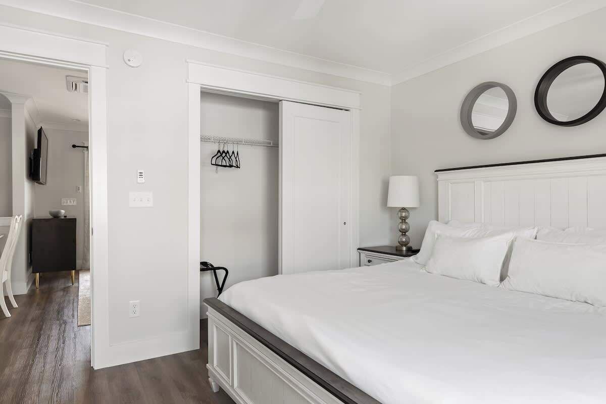 A bedroom with a bed, a nightstand, a lamp, a wardrobe, and a mirror on the wall.