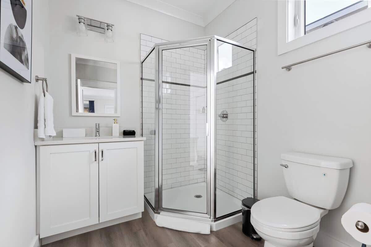 Une salle de bain moderne avec une douche à parois de verre, des toilettes blanches et un meuble-lavabo avec des placards.