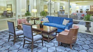 A hotel lobby with a blue sofa, armchairs, a coffee table, and a glass partition reflecting the interior.