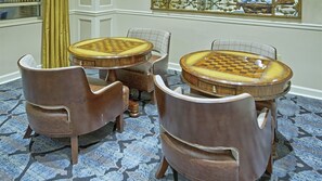 A room with a checkered table and four chairs, a patterned carpet, and a decorative wall piece.