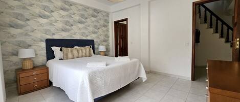 A bedroom with a bed, nightstands, a wooden dresser, a stone-patterned wall, and a staircase.