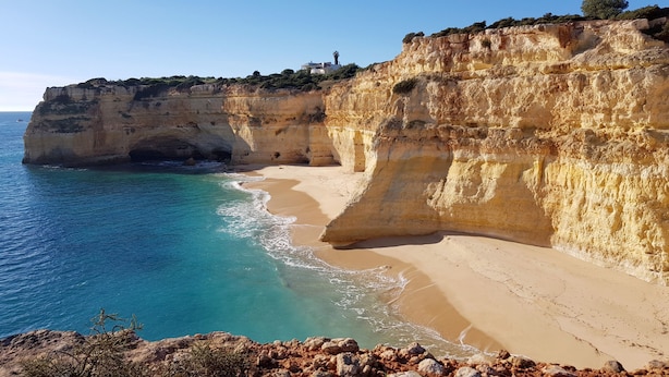 Eine Küstenlandschaft mit Klippen, einem Sandstrand und einem klaren, blauen Meer.