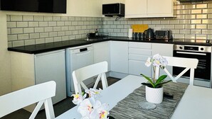 A modern kitchen with white cabinets, a black countertop, and a built-in microwave. There is a dining table with white chairs and a vase of orchids.