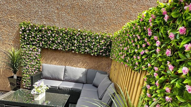 An outdoor seating area with a sofa and tables, surrounded by lush greenery and flowers.