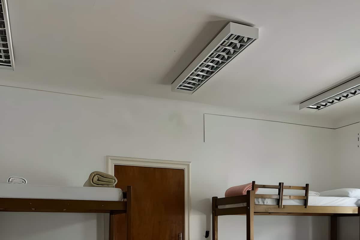 Ett rum med två våningssängar, en trädörr och ett vitt tak med ventilationsgaller.