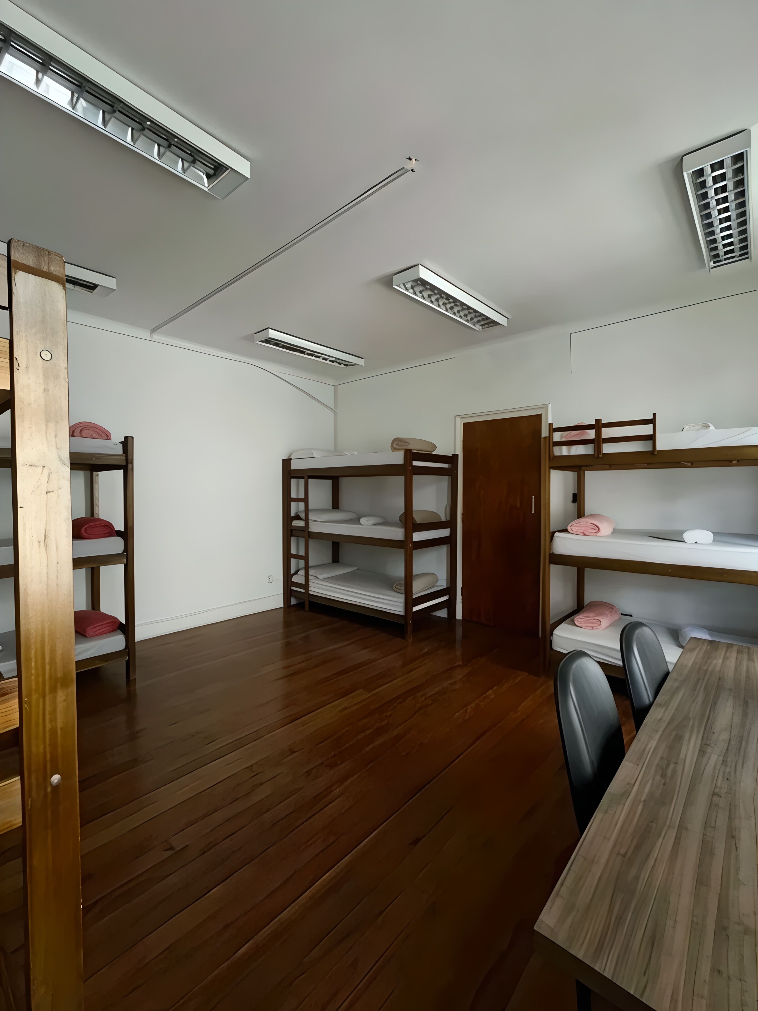 Una habitación con literas, una mesa de madera y luces en el techo.