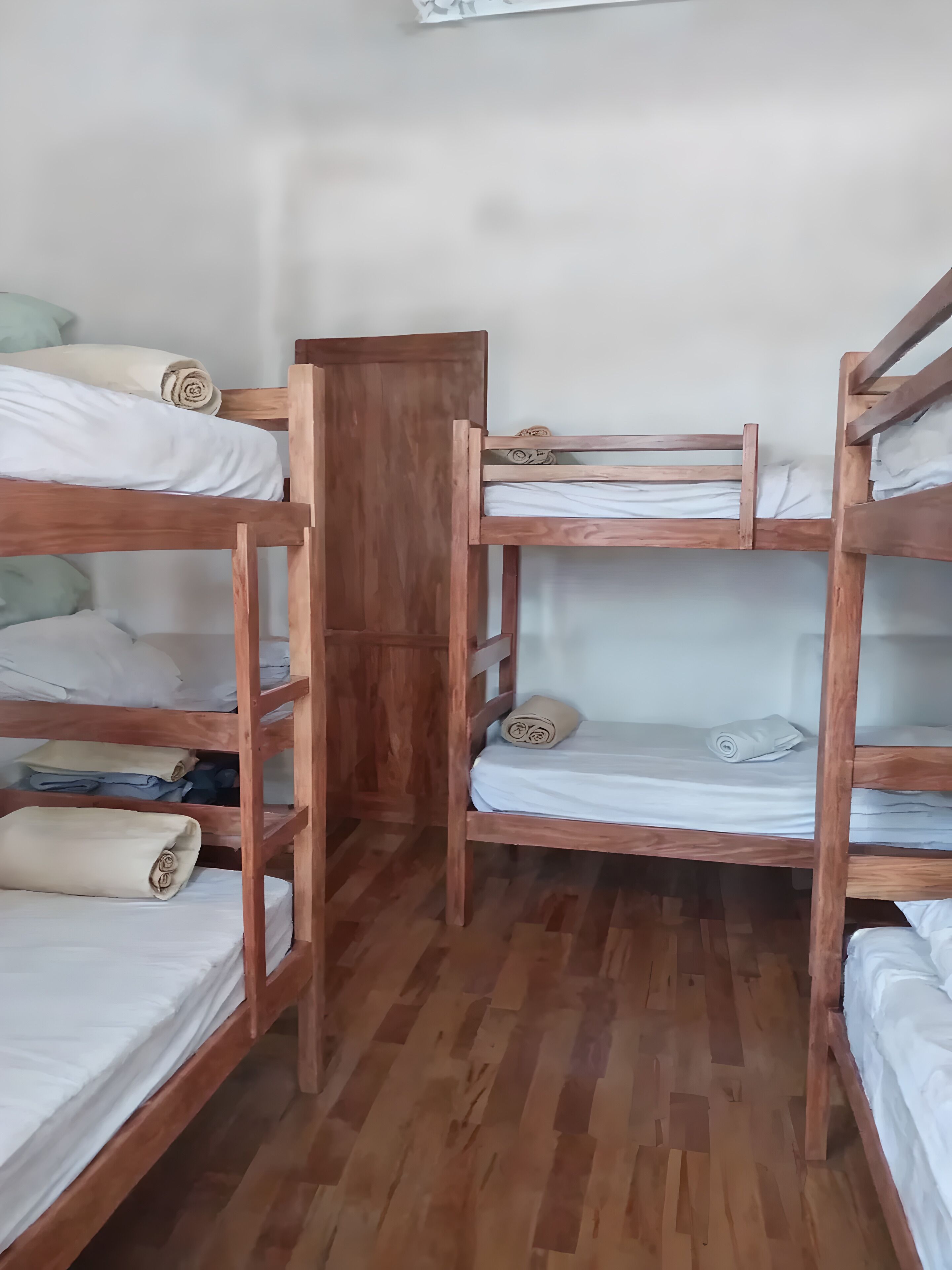 A room with four wooden bunk beds, each with white bedding and rolled towels.