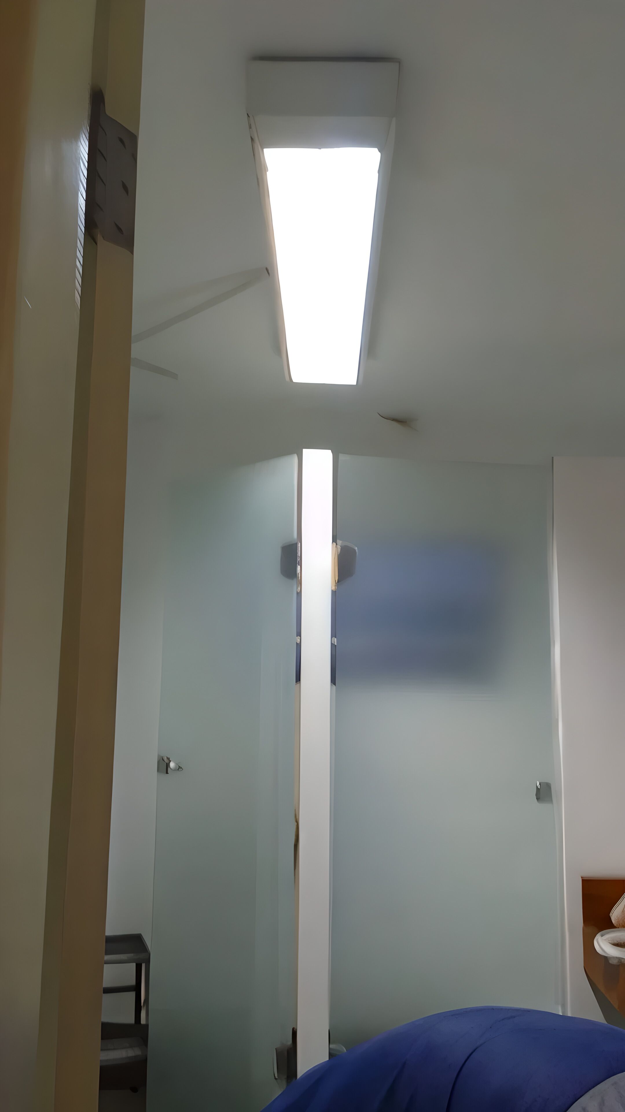 A hotel room with a skylight, a bed, a small table, and a mirror.
