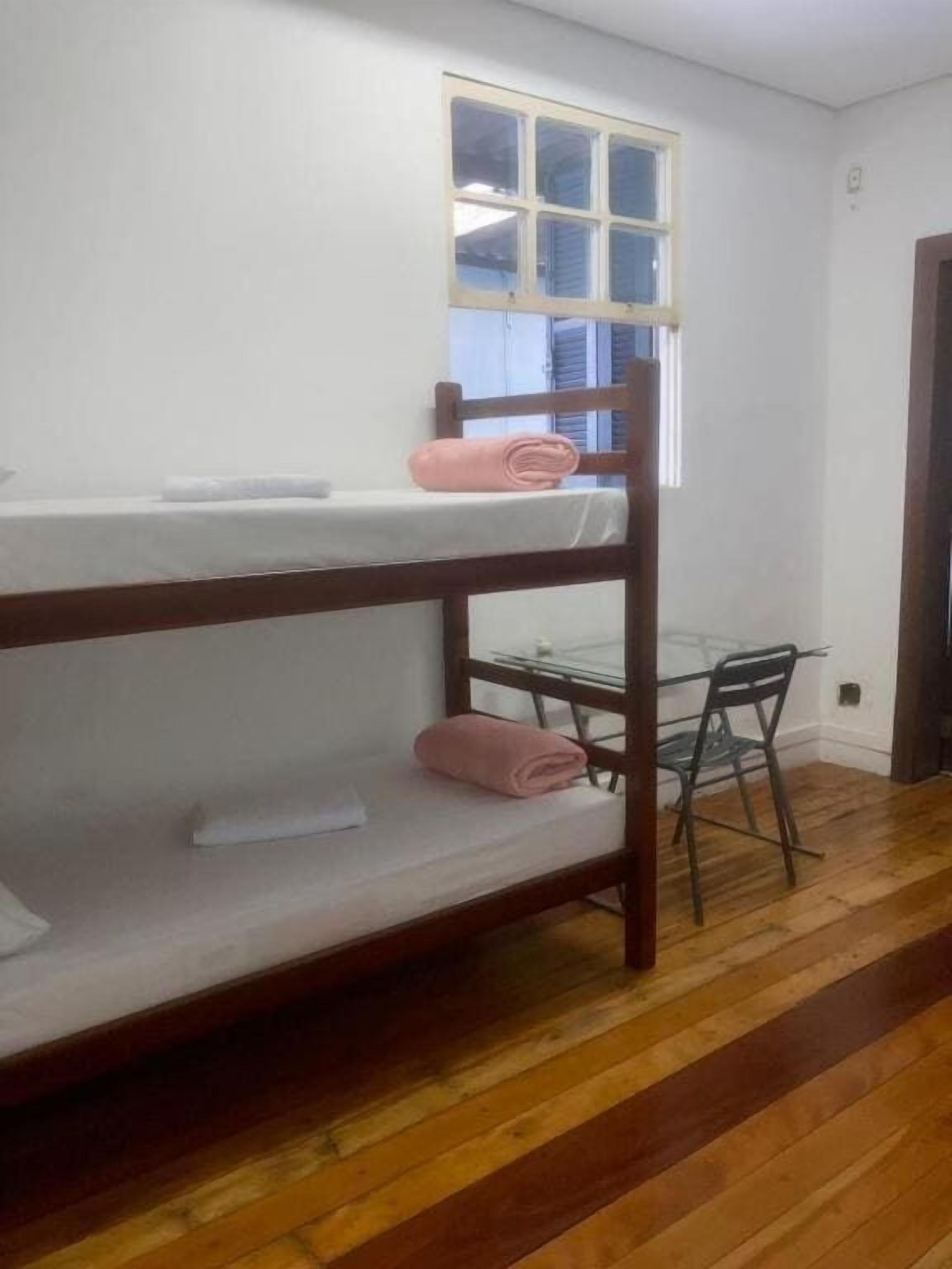 A bunk bed with a window above it, a small table, and a chair.