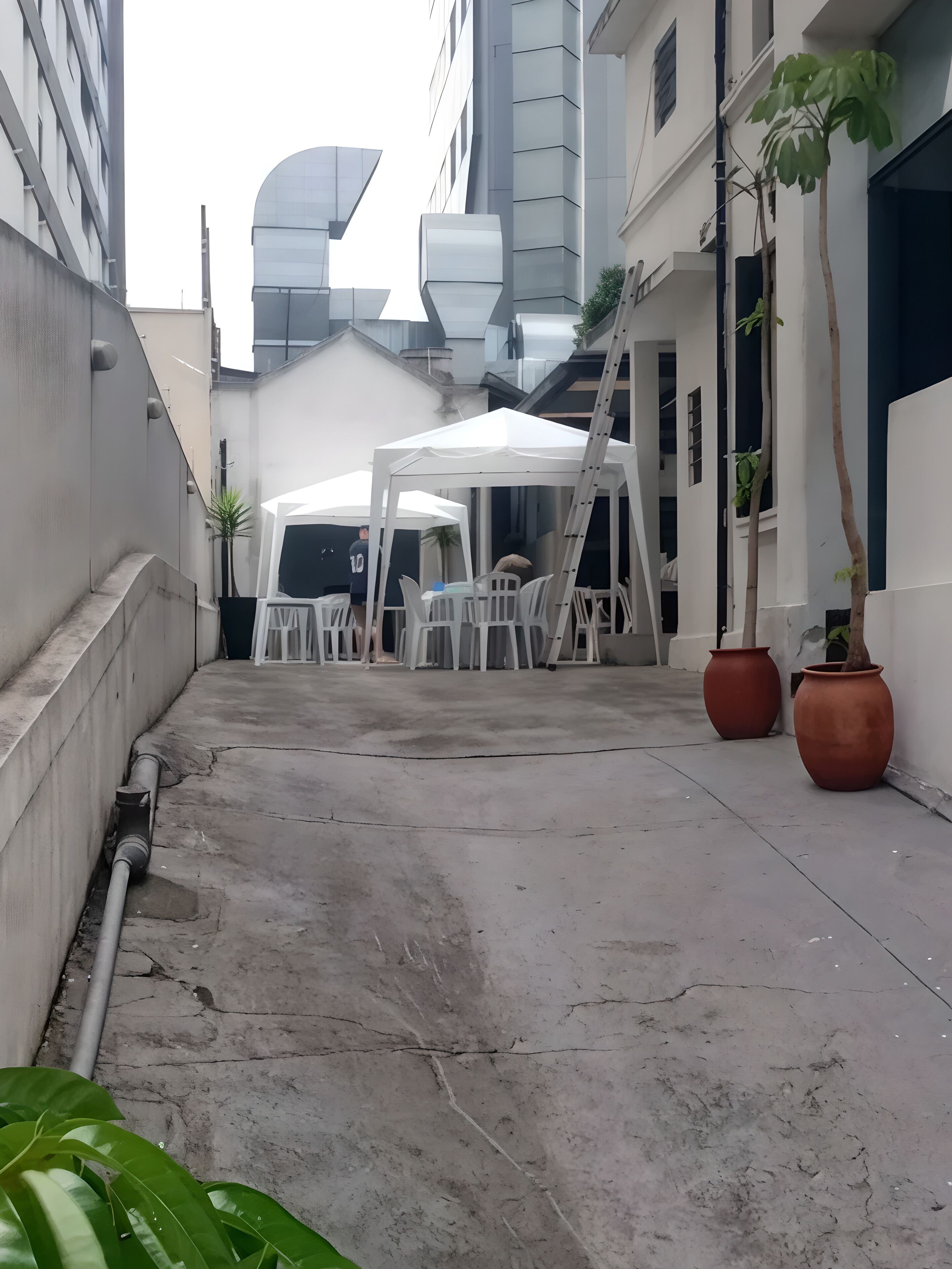 Une cour avec une tente blanche, des chaises blanches et des plantes en pot.