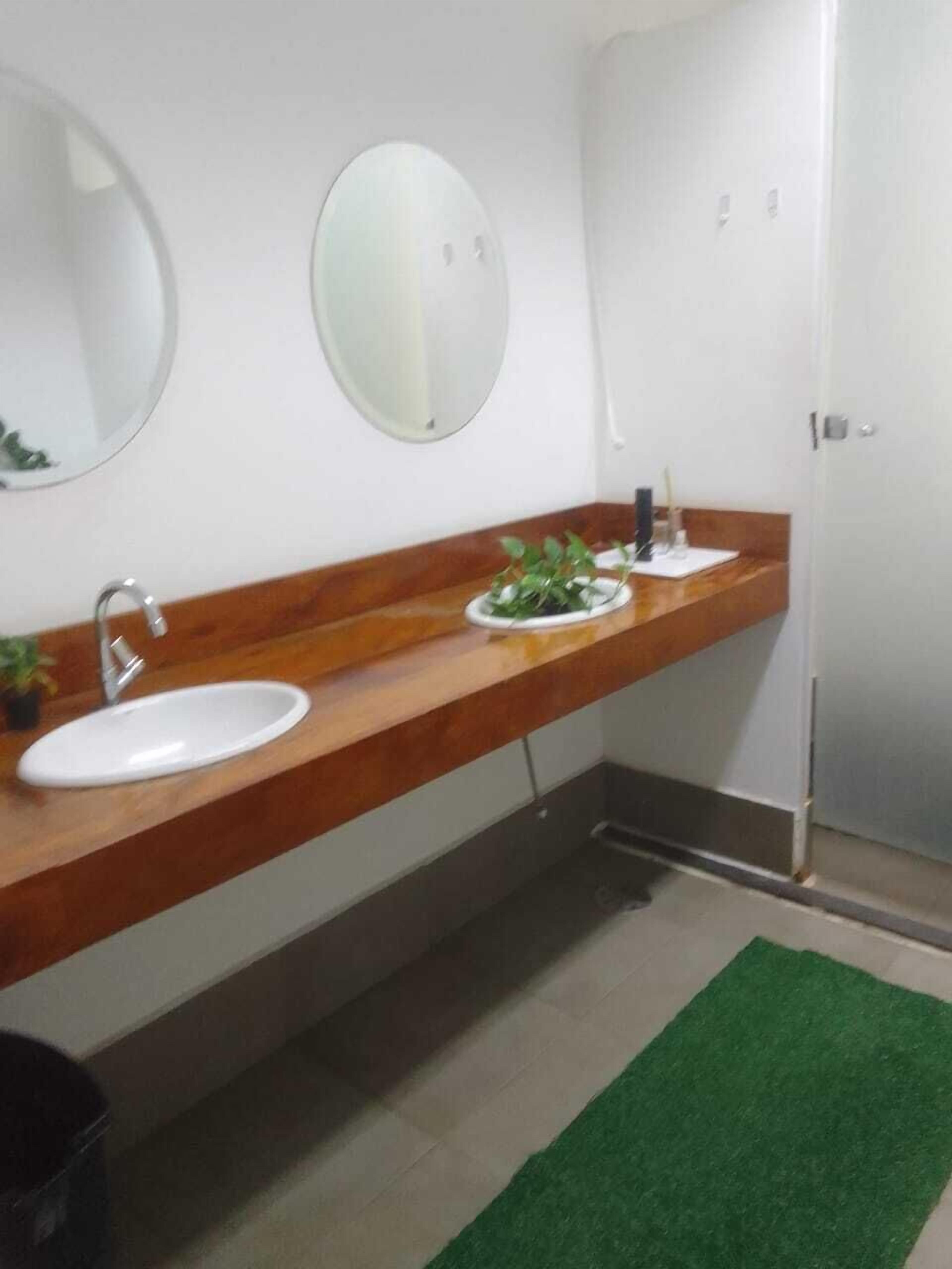 Un baño con lavamanos blanco, tocador de madera, espejo y alfombra verde en el suelo.