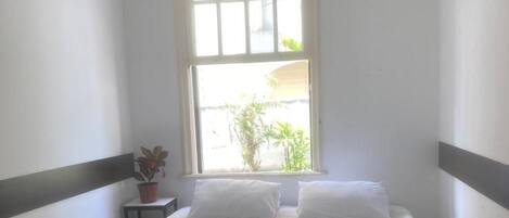 A bedroom with a large window, a bed with white linens, and a small potted plant.
