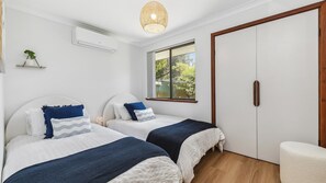 A bedroom with two beds, a wardrobe, a window with a view, and an air conditioning unit.