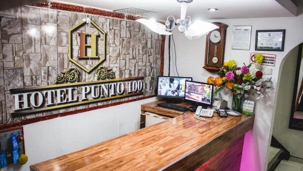 Un mostrador de recepción de hotel con un fondo de pared de piedra, un reloj y un arreglo floral.