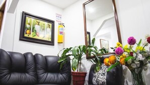 Una habitación con un sofá de cuero negro, una planta en maceta, un florero con flores, un cuadro enmarco y un espejo.
