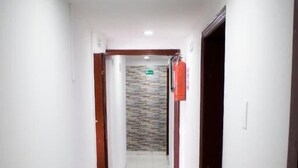 Un pasillo estrecho y bien iluminado, con paredes blancas y suelo de baldosas, que conduce a una habitación con un muro de acento de piedra.