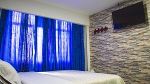 Un dormitorio con una cama, un televisor montado en la pared y una ventana con cortinas azules.