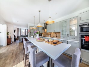 Cozinha moderna com ilha central, banquetas, iluminação pendente e vista para área externa.