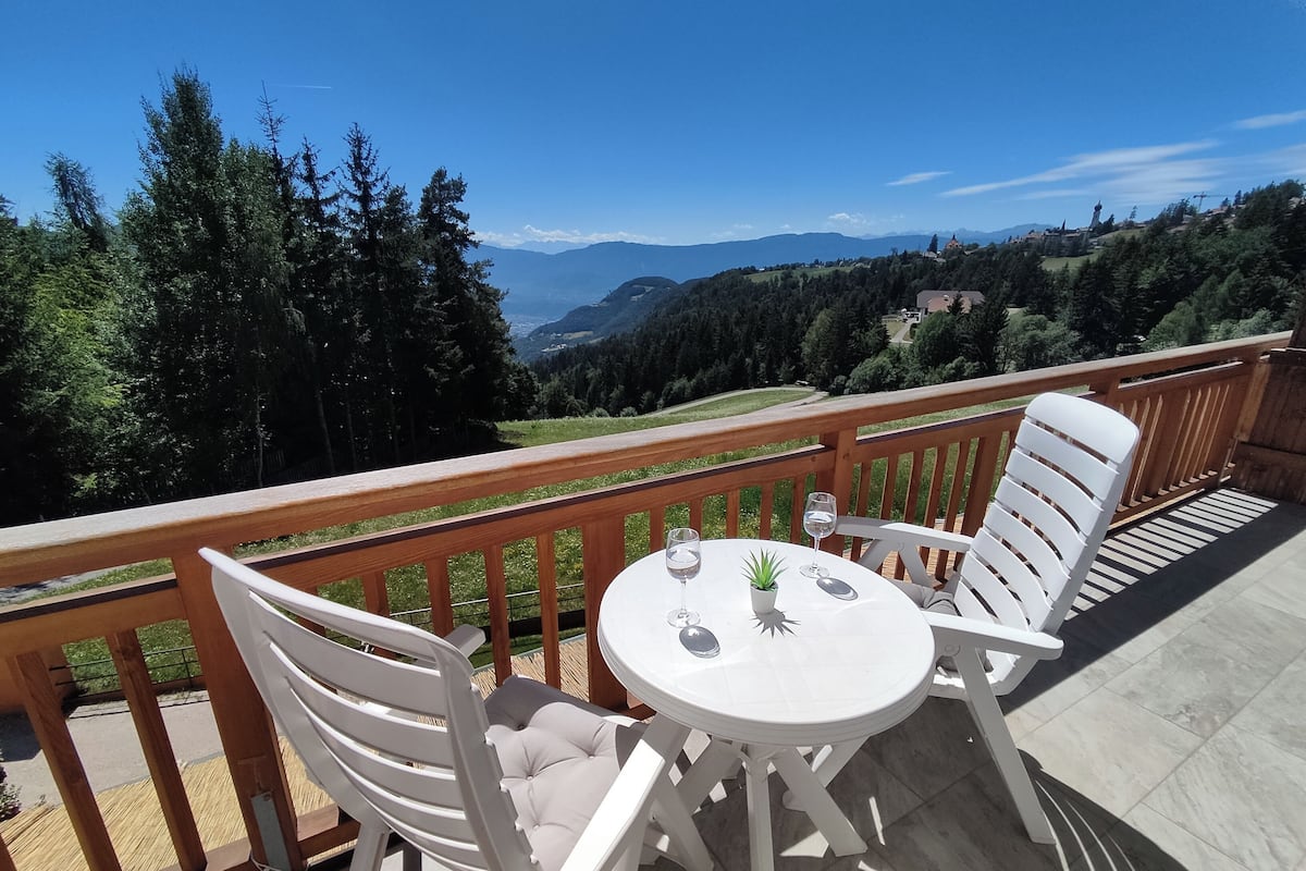 A balcony with a table and chairs, overlooking a mountainous landscape.
