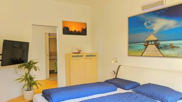 Ein Schlafzimmer mit einem Bett, einem Kleiderschrank, einer Topfpflanze und einem Bild von einer Strandansicht.
