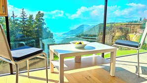 A balcony with a table and two chairs, overlooking a scenic landscape with mountains and a river. - Vidora Apartments (Renon)