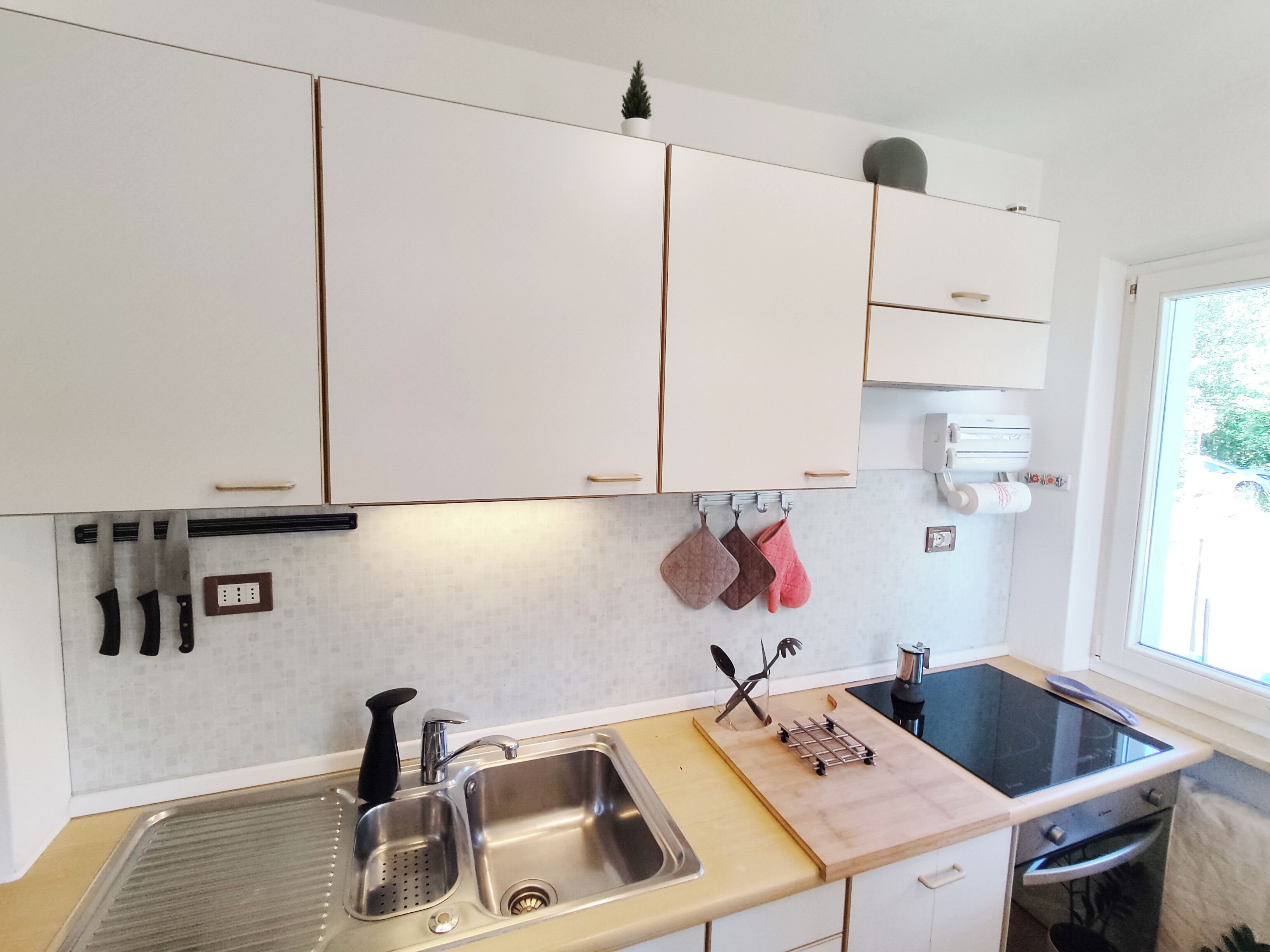 A modern kitchen with white cabinets, a stainless steel sink, a black stove, and a window providing natural light.