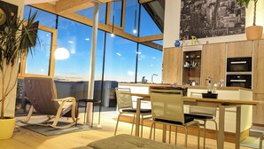A modern kitchen with large windows, wooden cabinets, and a dining area with chairs and a table. - Vidora Apartments (Renon)