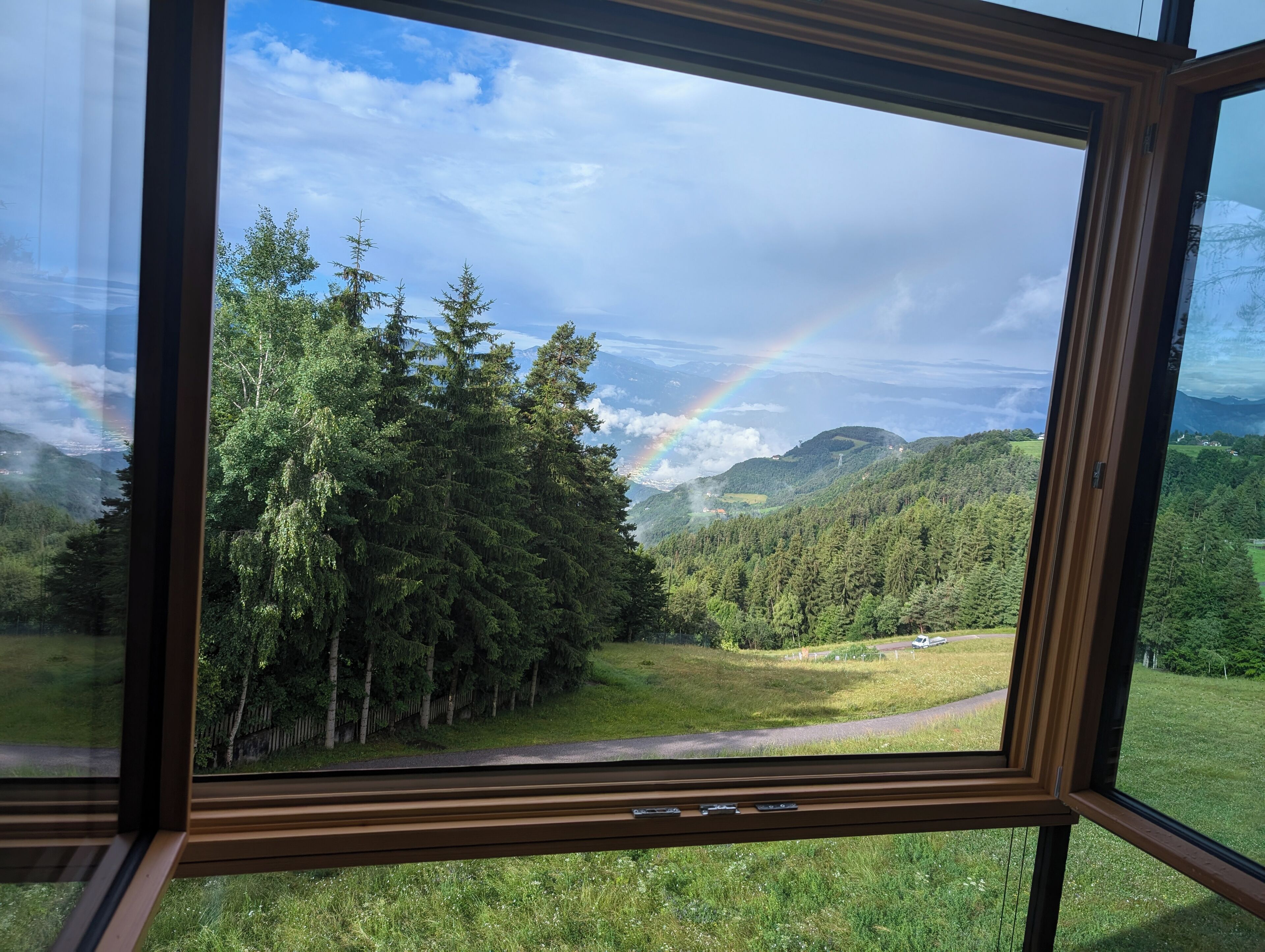 Paesaggio boschivo con arcobaleno visibile attraverso una finestra.