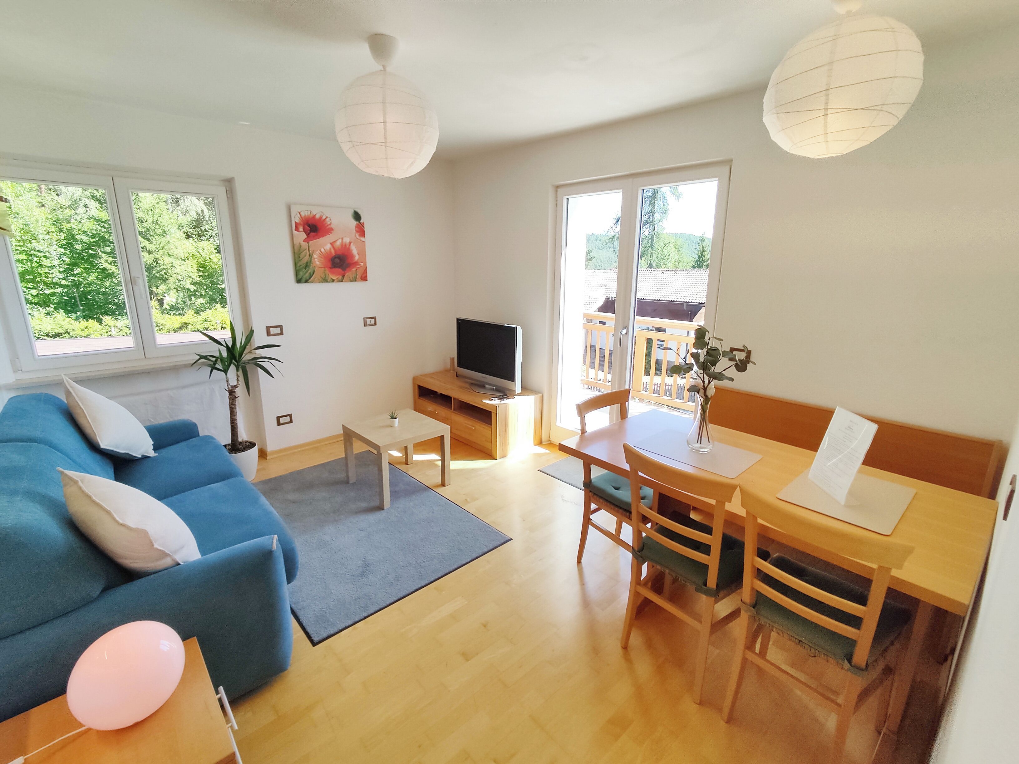 Een woonkamer met een blauwe bank, een bijzettafeltje, een televisie en een balkon met houten hekwerk.