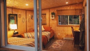 Una habitación de cabaña de madera con dos camas, una ventana y una silla.