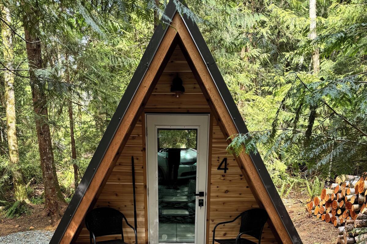 Una cabaña de madera con techo triangular, una puerta con el número 4 y dos sillas afuera.