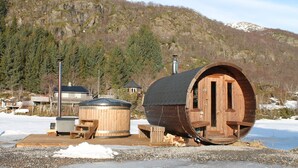 A wooden barrel-shaped building with a door and windows, a wooden deck, and a hot tub. - Lofoten Camp Storfjord (Vestvågøy)